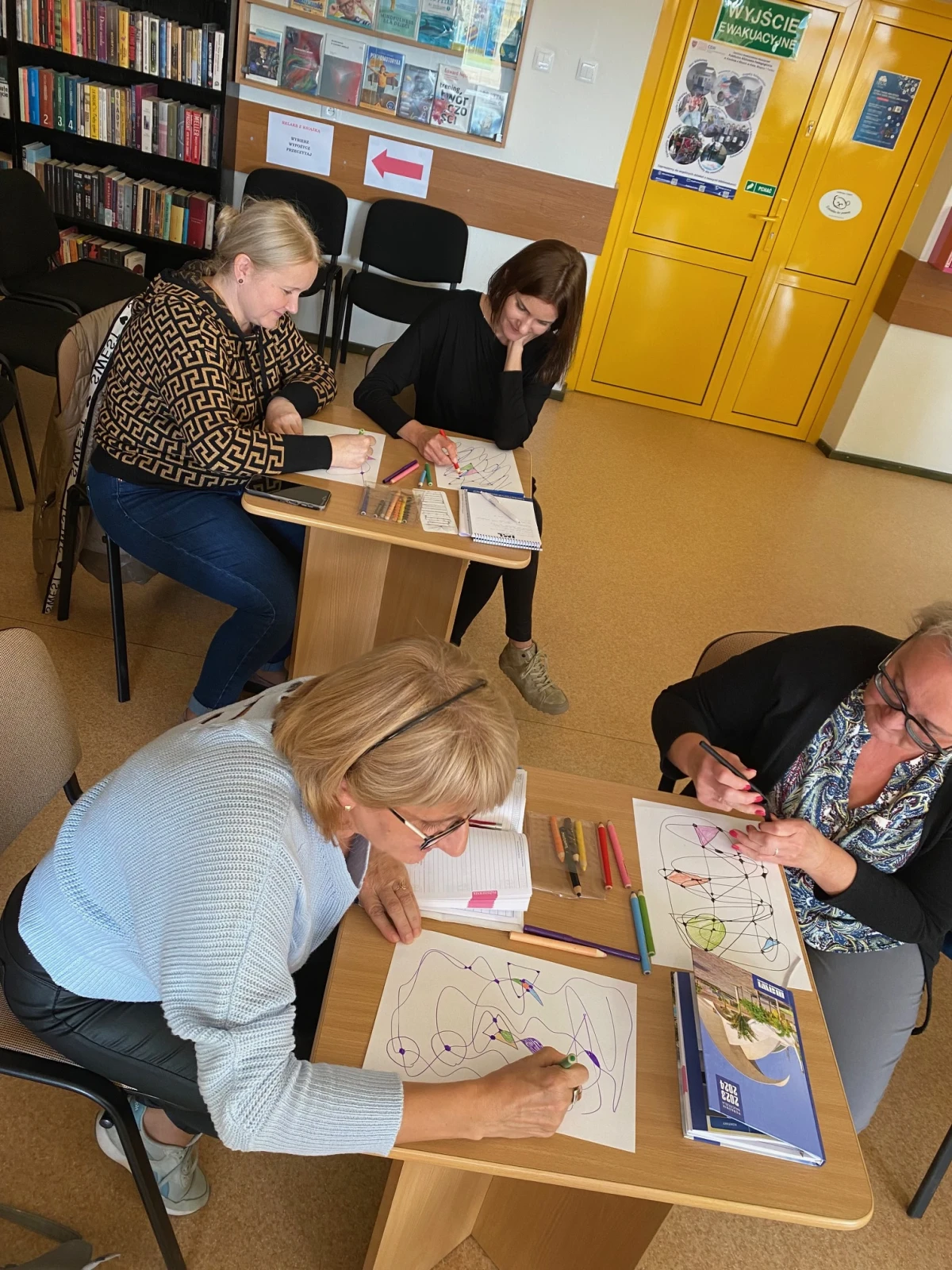 Zdjęcie przedstawia nauczycielki siedzące przy stolikach w bibliotece